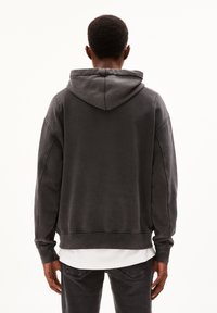 Šedá bavlněná mikina s velkou kapucí, volný střih a viditelné švy, doplněná o bílý spodní lem. Pohled zezadu.