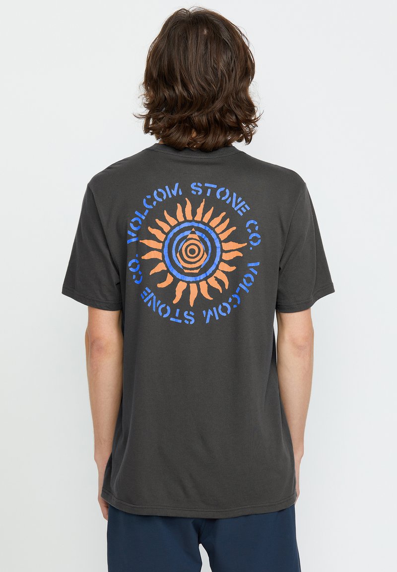T-shirt en coton gris foncé avec un graphique circulaire en bleu et orange, représentant un design de soleil avec des rayons et le texte "VOLCOM STONE CO."