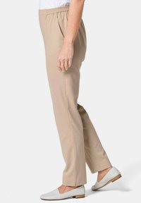 Pantalons beige à taille élastique avec une coupe droite, texture de tissu lisse et poches latérales. Associés à des chaussures plates blanches.