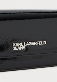 Fekete lakk bőr pénztárca, ezüst színű, "KARL LAGERFELD JEANS" felirattal, visszazárt logóval, sima felülettel és elegáns dizájnnal.