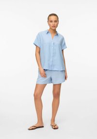 Camisa de botones de manga corta en azul claro con un cuello, combinada con pantalones cortos a juego. Tejido suave con una textura sutil y un corte relajado.