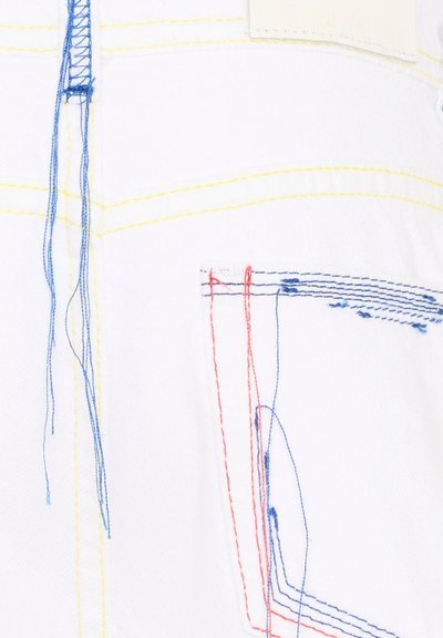 Tissu blanc avec des fils bleus, rouges et jaunes visibles et lâches ainsi que des lignes de couture, montrant une texture textile détaillée et un design de couture.