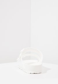 Sandalie albe cu talpă plată, material moale la atingere și design cu curea ajustabilă. Stil minimalist, fără elemente de prindere vizibile sau modele.