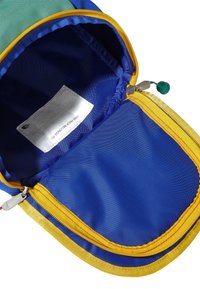 Krāsains mugursomas iekšpuse zilā audumā ar dzeltenu rāvējslēdzēju. Tajā ir etiķete un zaļš rāvējslēdzēja vilcējs. Gluda tekstūra, plašs atvērums.