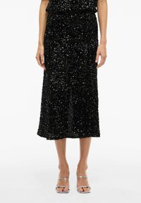 Robe midi noire à sequins avec une taille cintrée et une jupe évasée. La robe présente une surface texturée et réfléchissante, accompagnée de talons argentés à lanières.