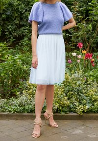 Lichtpaarse gebreide top met korte pofmouwen, gecombineerd met een luchtige lichtblauwe tule rok. Accessoires zijn gouden haksandalen.