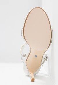 Vue unique d'une sandale blanche à talon haut ornée de strass et d'une petite pierre bleue sur la cambrure, taille 37, sur un fond blanc.