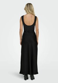 Schwarzes Abendkleid mit tiefem Rückenausschnitt, tailliertem Oberteil und schwingendem Rock. Hergestellt aus einem glatten, leichten Stoff. Sichtbare Stiefel mit Absatz.