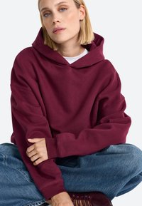 Bordeaux oversized hoodie met een elastische capuchon en geribbelde manchetten, gecombineerd met losse lichtblauwe jeans. Gladde stofstructuur.