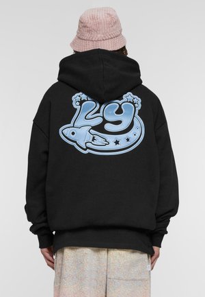 Svart hoodie med en stor blå grafik på baksidan som visar siffran "29", en raket och stjärnor. Materialet verkar mjukt och texturerat.