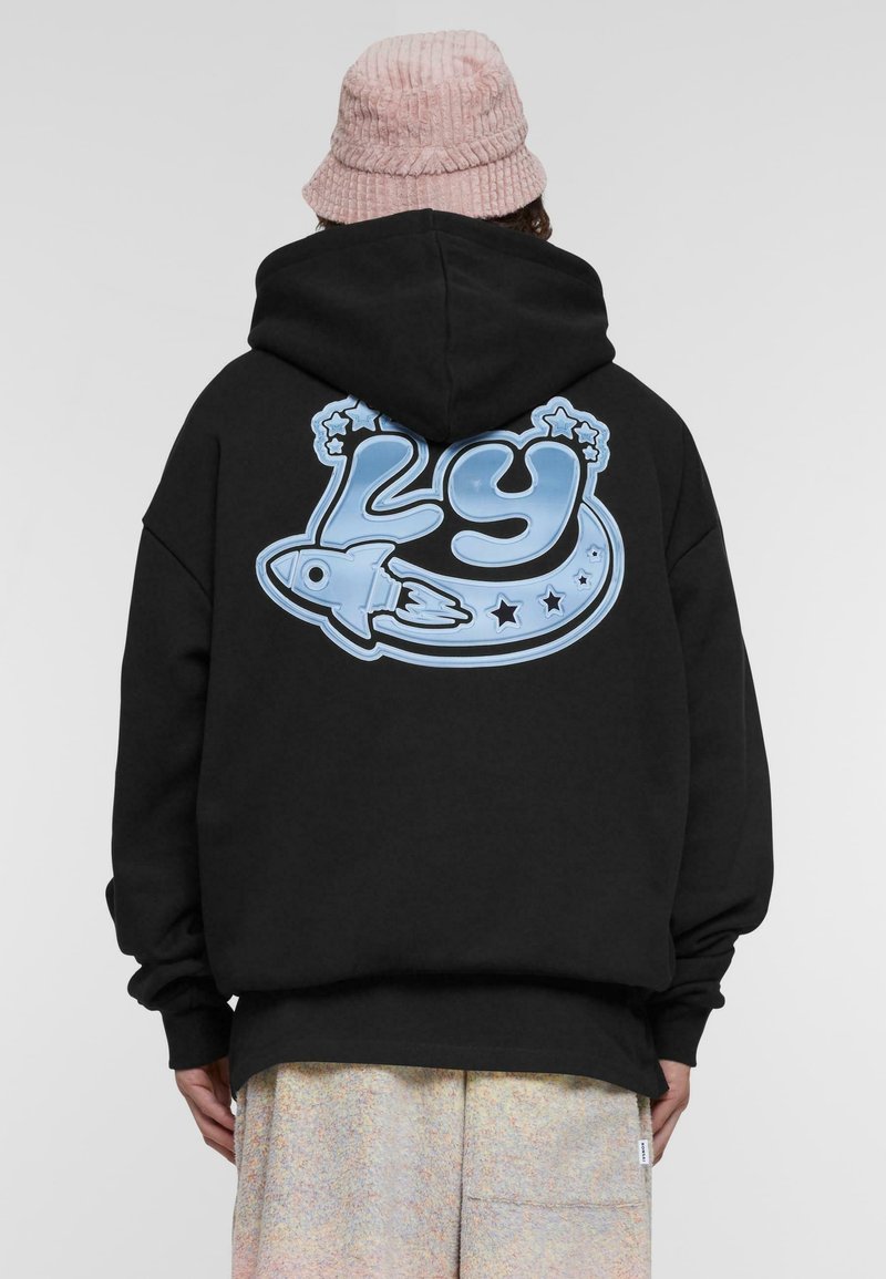 Sudadera negra con un gran gráfico azul en la parte trasera que muestra el número "29", un cohete y estrellas. El material parece suave y texturizado.