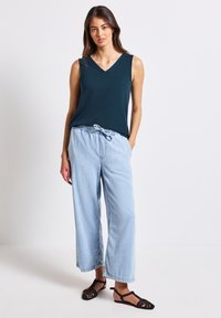 Turkusowa bezrękawnik z dekoltem w serek, w połączeniu z jasnoniebieskimi, luźnymi dżinsami i czarnymi sandałami na paski. Prosty design, luźny krój.