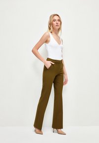 Olijfgroene op maat gemaakte broek met een gladde voorkant, zijzakken en een rechte pijp, gecombineerd met een witte mouwloze top.