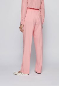 Světlé růžové kalhoty z volného, krémového materiálu s gumovým pasem, doplněné o bílé boty s černými akcenty.