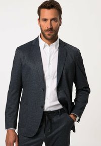 Blazer strutturato blu scuro con due bottoni, abbinato a una camicia bianca. Design slim fit, con taschino sul petto e pantaloni eleganti.