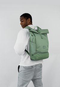 Zöld, felhajtható hátizsák, állítható vállpántokkal, elülső zsebbel és sima felülettel. A márkacímke az elülső alsó részén található.