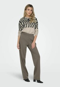 Suéter beige con rayas de cebra negras, combinado con pantalones verdes olivo de tiro alto y holgados. El modelo lleva botas de tacón negras.