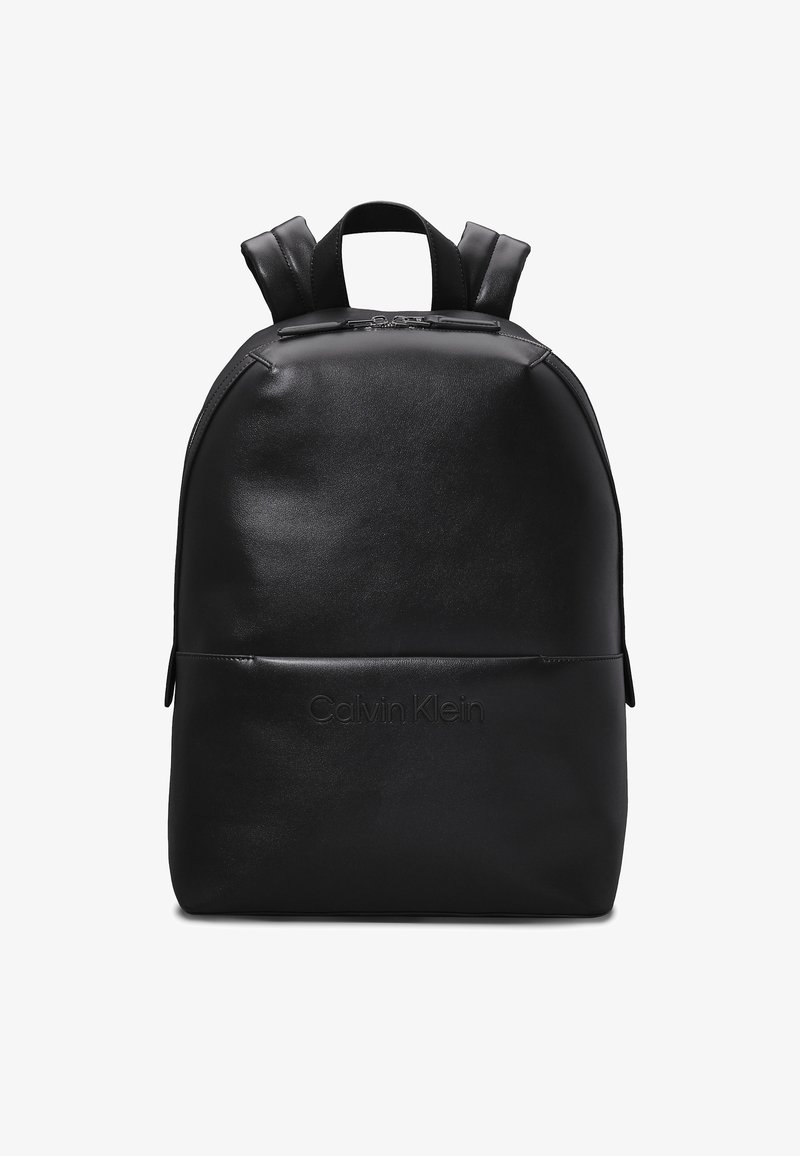 Zaino in pelle nera con forma arrotondata, dotato di spallacci regolabili e tasca con zip frontale. "Calvin Klein" impresso sul davanti.