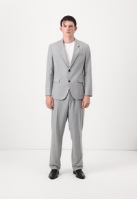 Gray pinstriped suit featuring a structured blazer with a notched lapel and matching trousers, paired with a plain white t-shirt and black shoes.