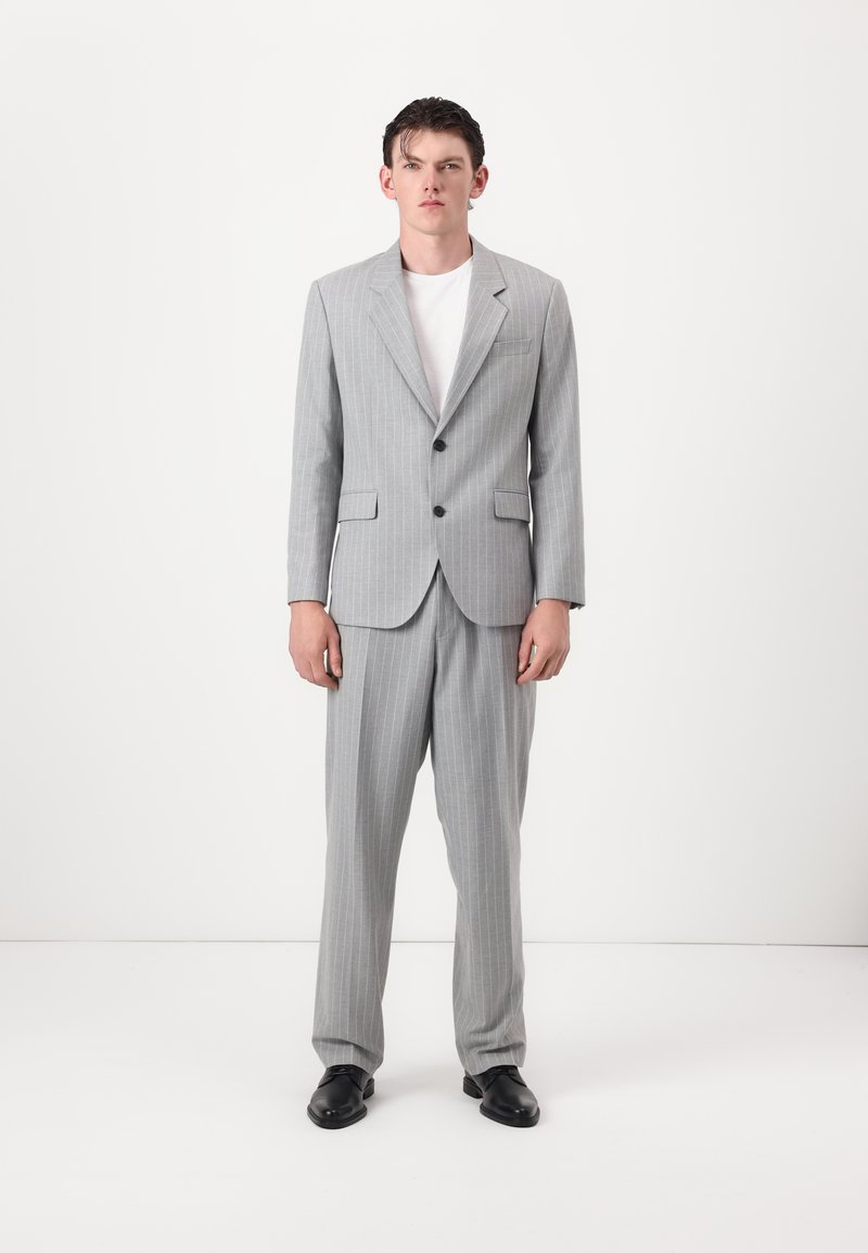 Gray pinstriped suit featuring a structured blazer with a notched lapel and matching trousers, paired with a plain white t-shirt and black shoes.