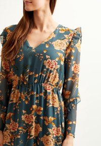 Abito floreale in tessuto teal, caratterizzato da scollo a V, maniche a volant e una vita elasticizzata. Motivo floreale nelle tonalità di giallo e rosa.