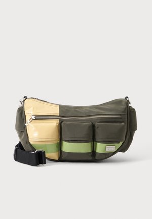 Sac bandoulière en vert olive et beige avec trois poches avant, fermeture éclair et bandoulière noire réglable sur fond blanc.
