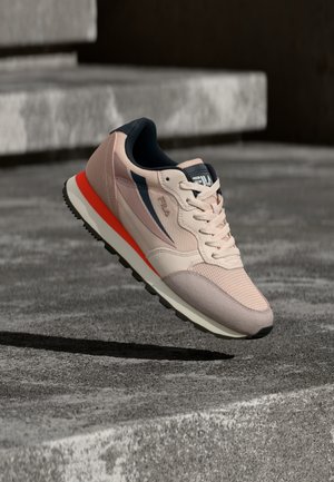 Ανοιχτό ροζ και ναυτικό αθλητικό παπούτσι με κόκκινη ρίγα στη σόλα, δεμένα κορδόνια, που αιωρείται πάνω από επιφάνεια από μπετόν κοντά σε σκαλοπάτια.