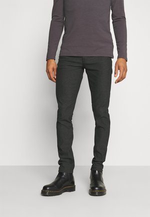 Slim-fit donkergrijze jeans van gestructureerde stof, gecombineerd met zwarte chelsea boots met gele stiksels. Lange mouw paarse shirt.