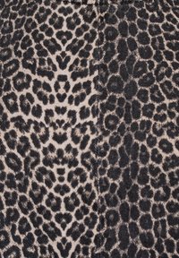 Gros plan sur un tissu à motif léopard noir et beige, présentant des formes de taches variées et un tissage texturé.