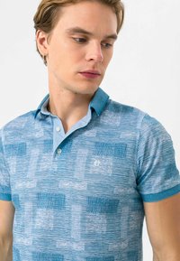 Kortærmet polo shirt i gradient blå nuancer; har tekstureret mønster og kontrastfarvet krave; frontknapper og lille logo detalje.