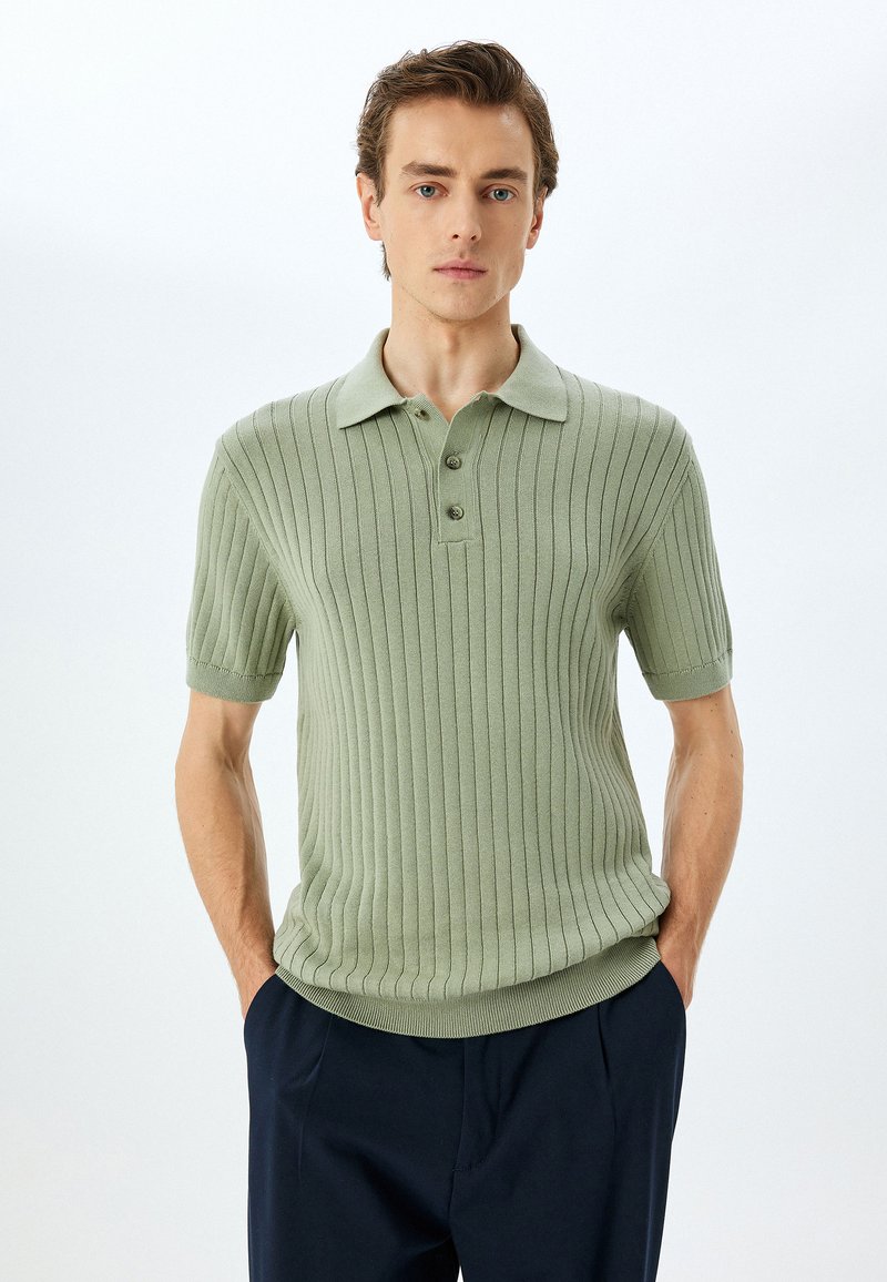 Texturerad, ribbad kortärmad polo t-shirt i dämpad grön, med krage och treknappsstängning. I kombination med mörka byxor.