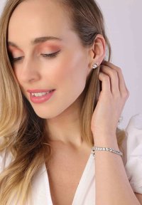 Ein Paar silberne Ohrringe mit kleinen, runden, klaren Steinen, dazu ein passendes Armband mit einer Reihe ähnlicher, funkelnder Steine.