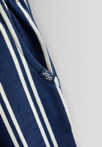 Blåt stof med hvide lodrette striber og en lille sort mærkat med teksten "JoJo" syet nær en søm.