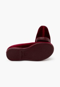 Zapato de terciopelo burdeos con punta redonda, tacón bajo y suela de goma texturizada. Presenta costuras decorativas y una marca en relieve en la suela.