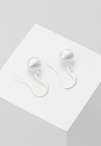 Silver hook earrings featuring round, matte finish, silver pearls. The hooks are elongated and curved for secure fastening.
