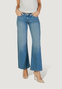 Jeans a gamba larga di un blu chiaro con vita alta, chiusura con bottone e tasche, abbinati a scarpe con tacco nudo.
