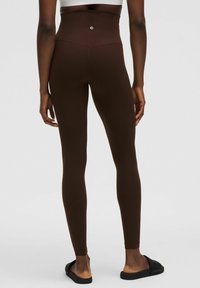 Leggings marron taille haute en matériau extensible, avec une texture lisse et un accent de logo à la taille arrière.