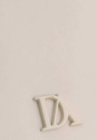 Superficie de color crema con un logo "DA" en relieve y brillante de color blanco. Textura suave con un ligero brillo y un diseño minimalista.