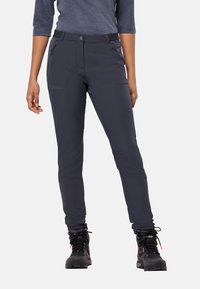 Pantaloni da outdoor in tessuto elastico nero con vestibilità slim. Presentano tasche laterali e chiusura con bottone. Indossati con stivali da escursione neri.
