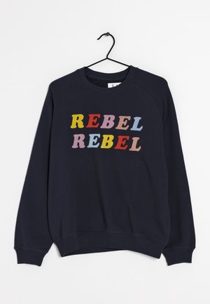 Navy blue sweatshirt with colorful letters spelling "REBEL REBEL" hanging on a black hanger against a white background.