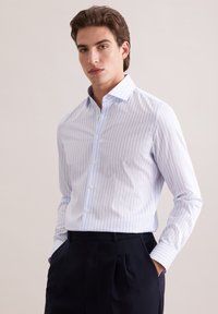 Jasnoniebieska i biała koszula w paski z długim rękawem, z kołnierzem w szpic, zapinana na guziki z przodu oraz standardowymi mankietami, w zestawieniu z ciemnogranatowymi spodniami.