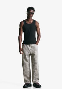 Schwarzes Tanktop, kombiniert mit hellgrauen, strukturierten, weit geschnittenen Hosen. Schwarze Schuhe mit pinken Schnürsenkeln und runde Sonnenbrillen runden den Look ab.