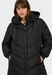 Black padded coat with a hood, featuring chevron quilted pattern, front zipper, and knit cuffs. Material appears smooth and lightweight.