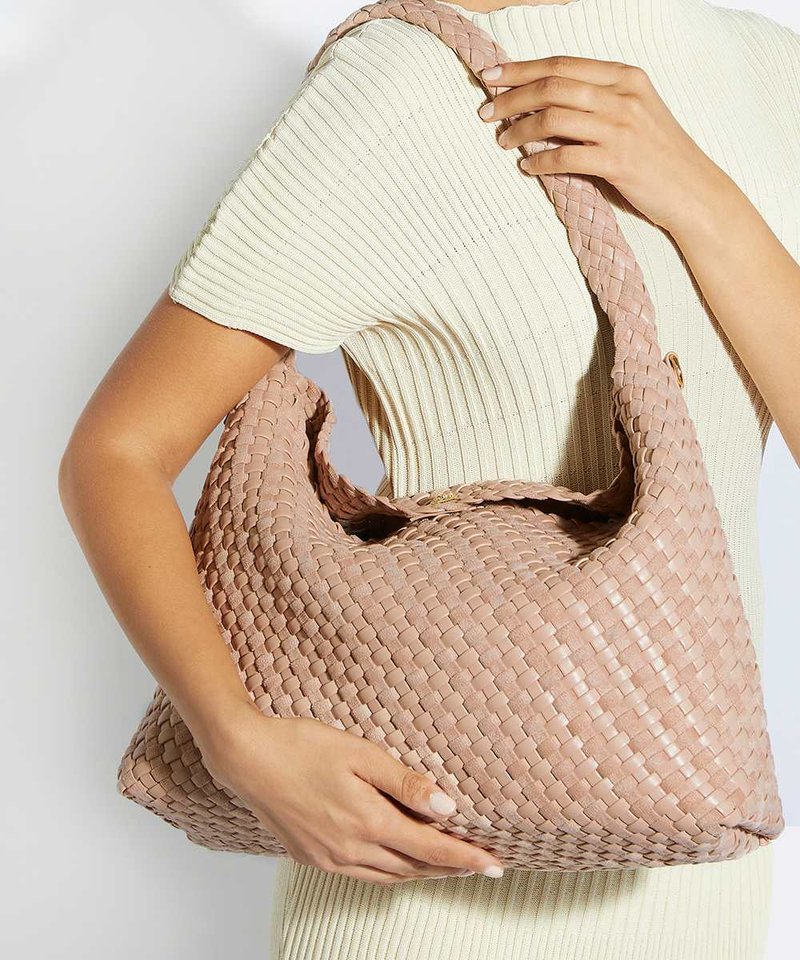 Personne portant un haut crème côtelé à manches courtes tenant un grand sac à main tissé rose pâle avec une bandoulière tressée sur l'épaule