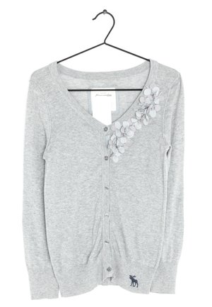 Cardigan gris clair boutonné avec des ornements floraux ronds sur l'épaule gauche et un petit logo sombre d'élan près de l'ourlet, suspendu à un cintre noir.