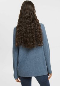 Ljusblå oversized tröja, ribbad fåll, mjuk textur, med långa ärmar och avslappnad passform, bärs över mörka jeans.