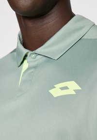 Light green polo shirt made of smooth fabric features a contrasting light yellow logo on the chest and a buttoned collar.