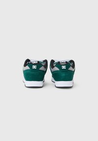 Grüne Wildledersneaker mit schwarzen und grauen Akzenten, weißen Sohlen, gepolsterten Kragen und einem Logo-Detail auf der Rückseite. Entwickelt für Komfort und Langlebigkeit.