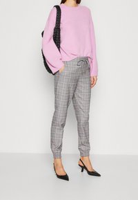 Light pink knitted sweater with long sleeves, paired with gray plaid trousers featuring an elastic waistband and ankle cuffs, and black heels.