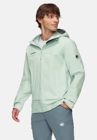 Helle mintgrüne wasserdichte Jacke mit Kapuze, Reißverschluss vorne, schwarzen Akzenten und Logo am Ärmel; entworfen für Outdoor-Aktivitäten.